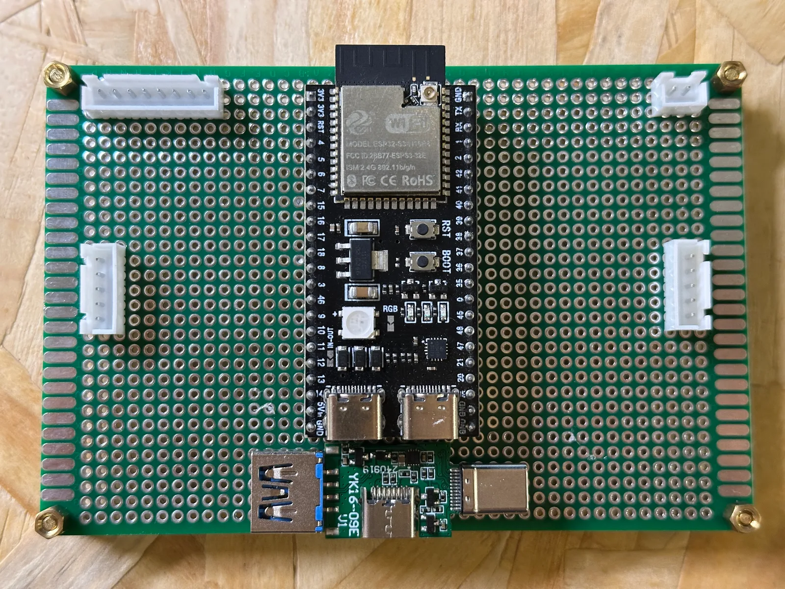 A hand-soldered prototype board with a microcontroller and rows of connectors on a workbench