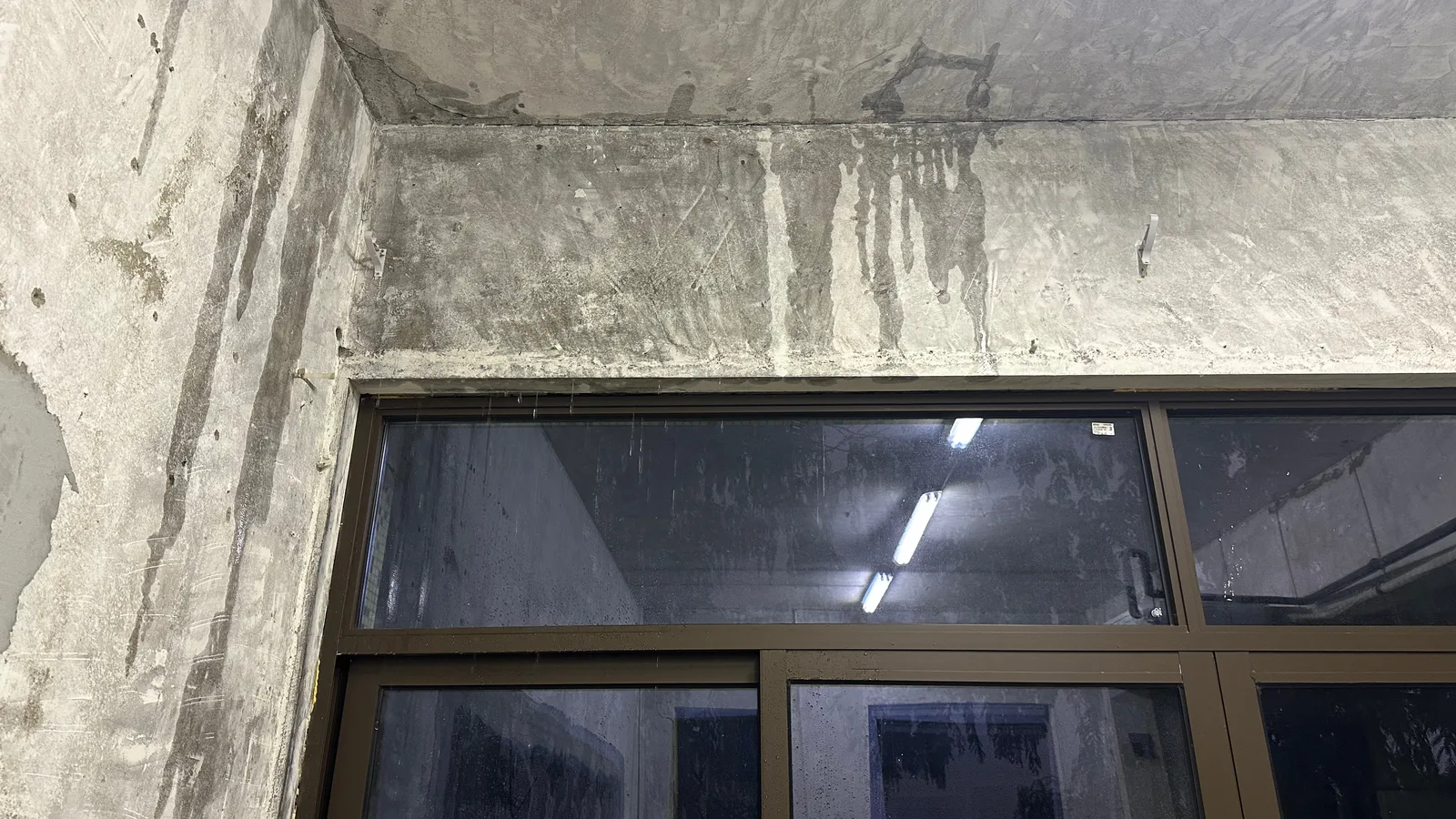 Water stains running down a concrete wall above a dark window at night
