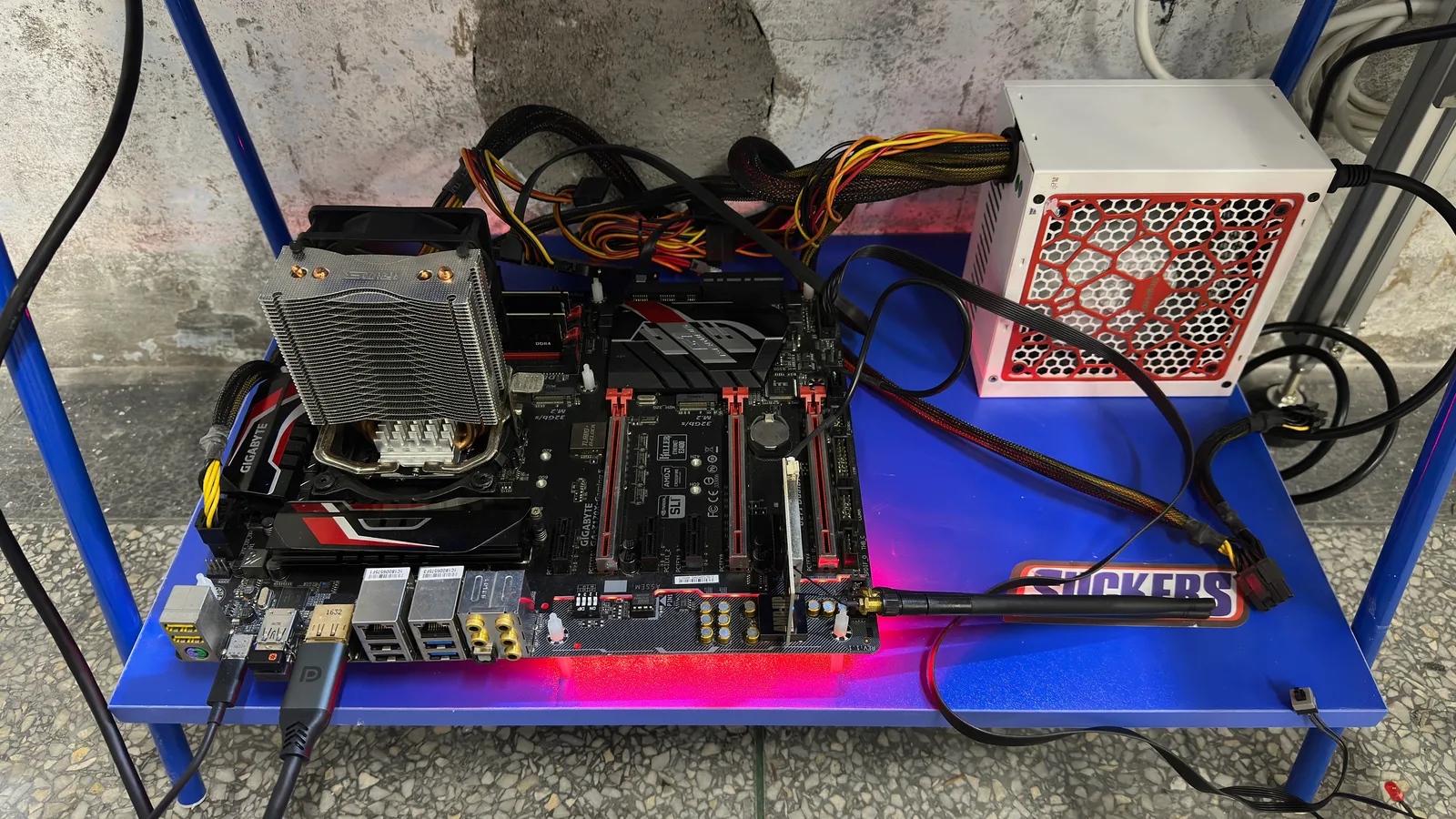 A bare computer motherboard with a cooler and a power supply on an open blue metal shelf