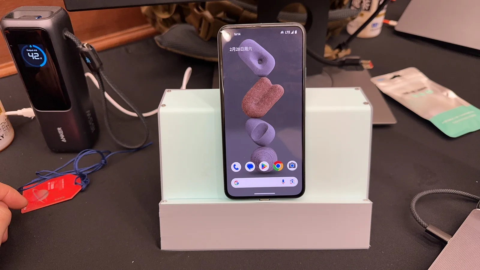 A phone standing in a white printed dock on a dark desk, with a small display box beside it